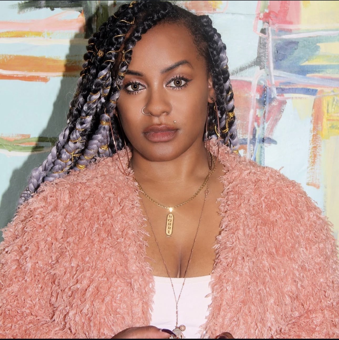 Portrait of Bobbi Makeda in a pink coat against an abstract painting