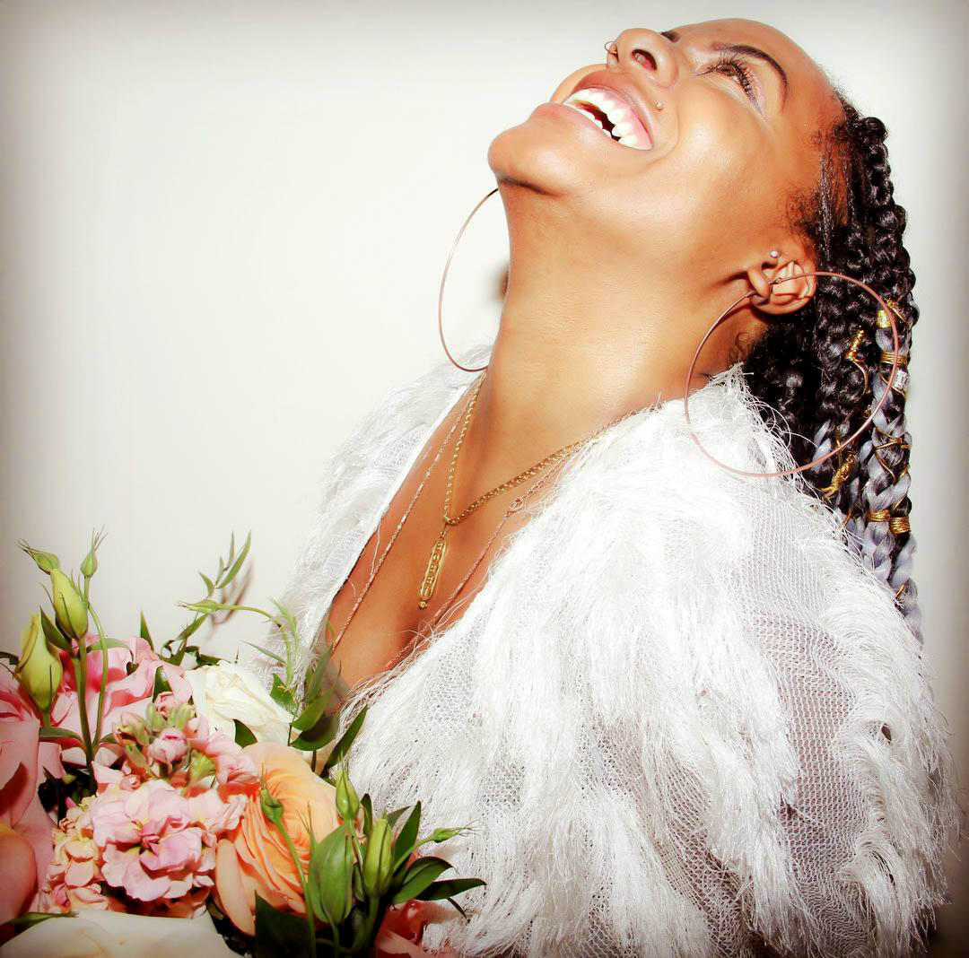 Bobbi Makeda laughing, wearing a white feather jacket and holding a bouquet of roses