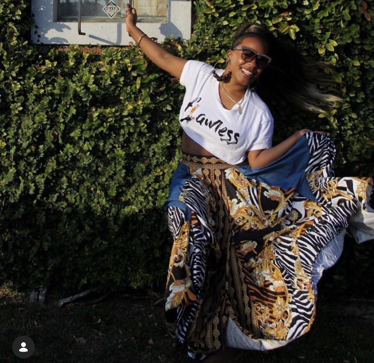 Bobbi Makeda in a flowing patterned skirt in front of a green hedge